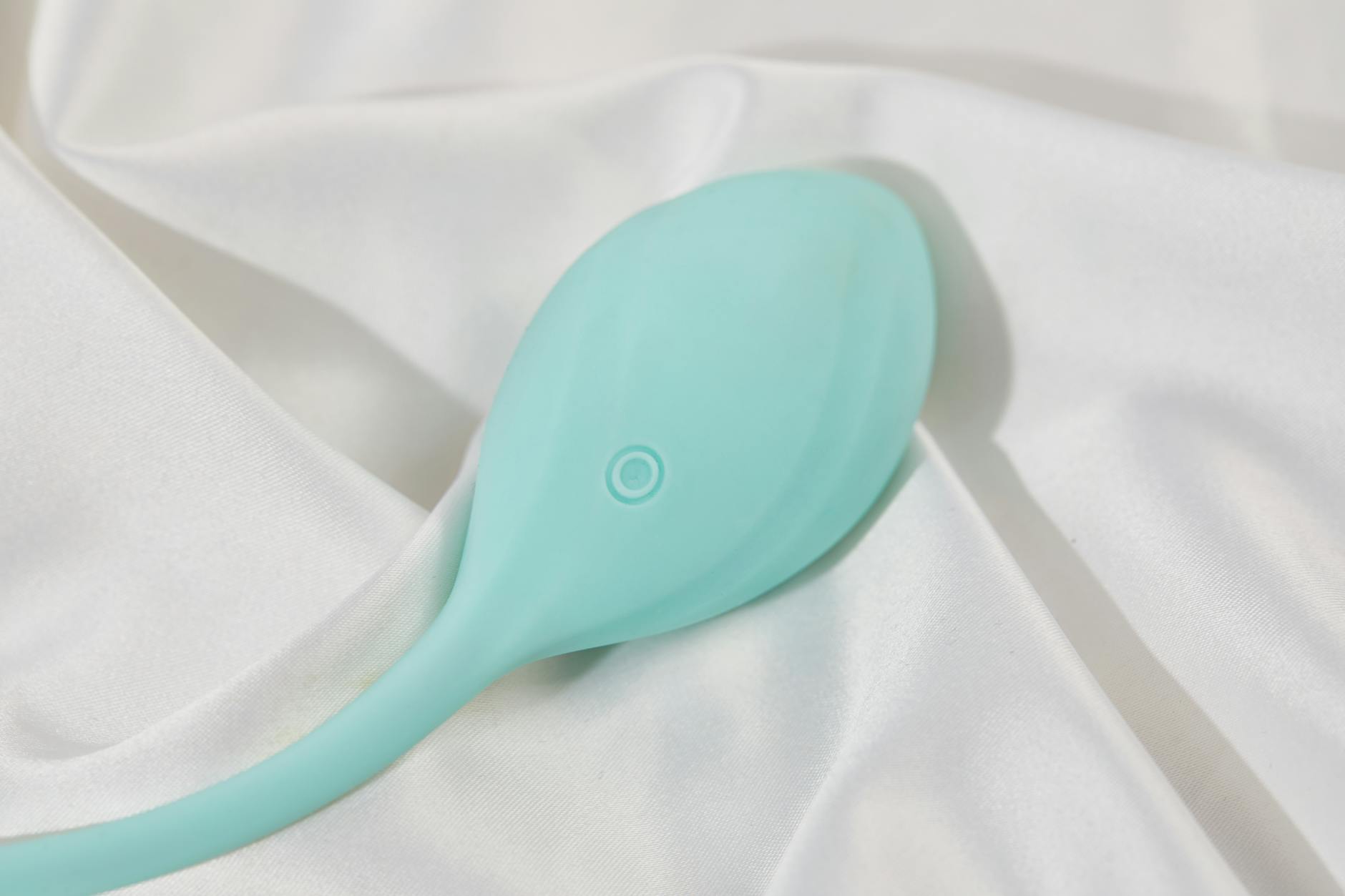 A sleek teal clitoral vibrator resting on soft white silk