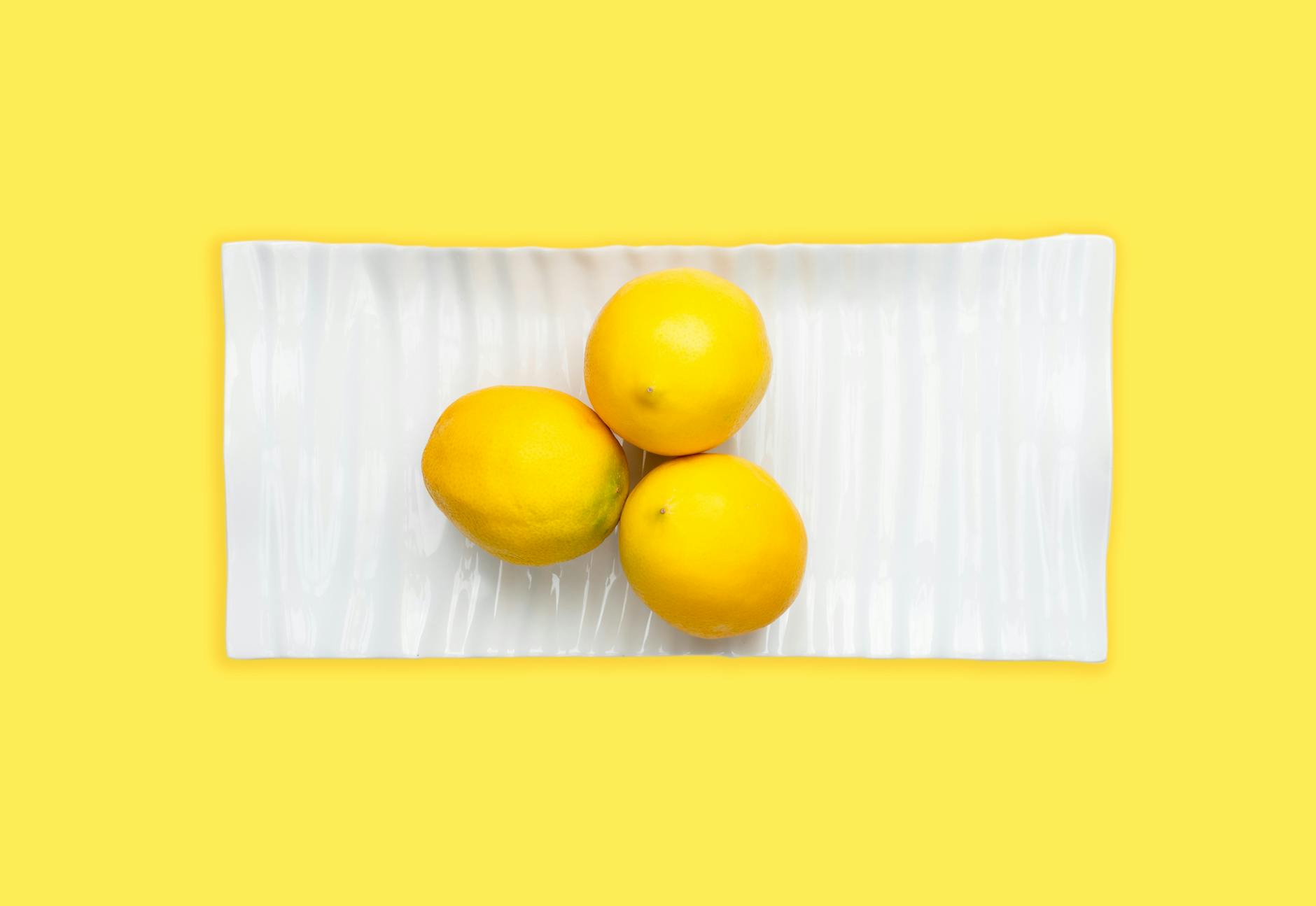 Fresh lemons on a white plate with yellow background, symbolizing freshness and reclaiming your own pleasure.
