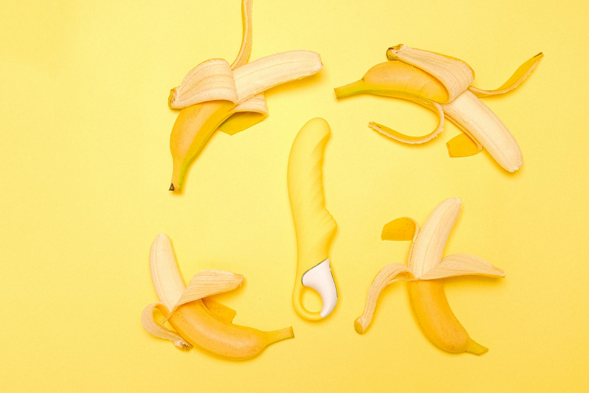 Yellow silicone lemon vibrator surrounded by peeled bananas on bright yellow background