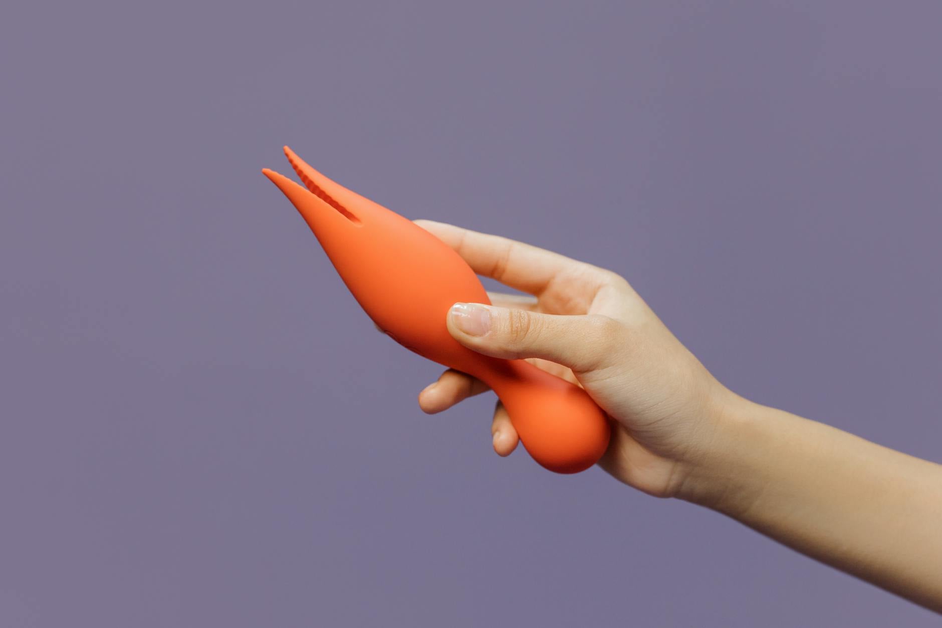 A hand holding a lemon-colored vibrator against a minimalistic purple backdrop.