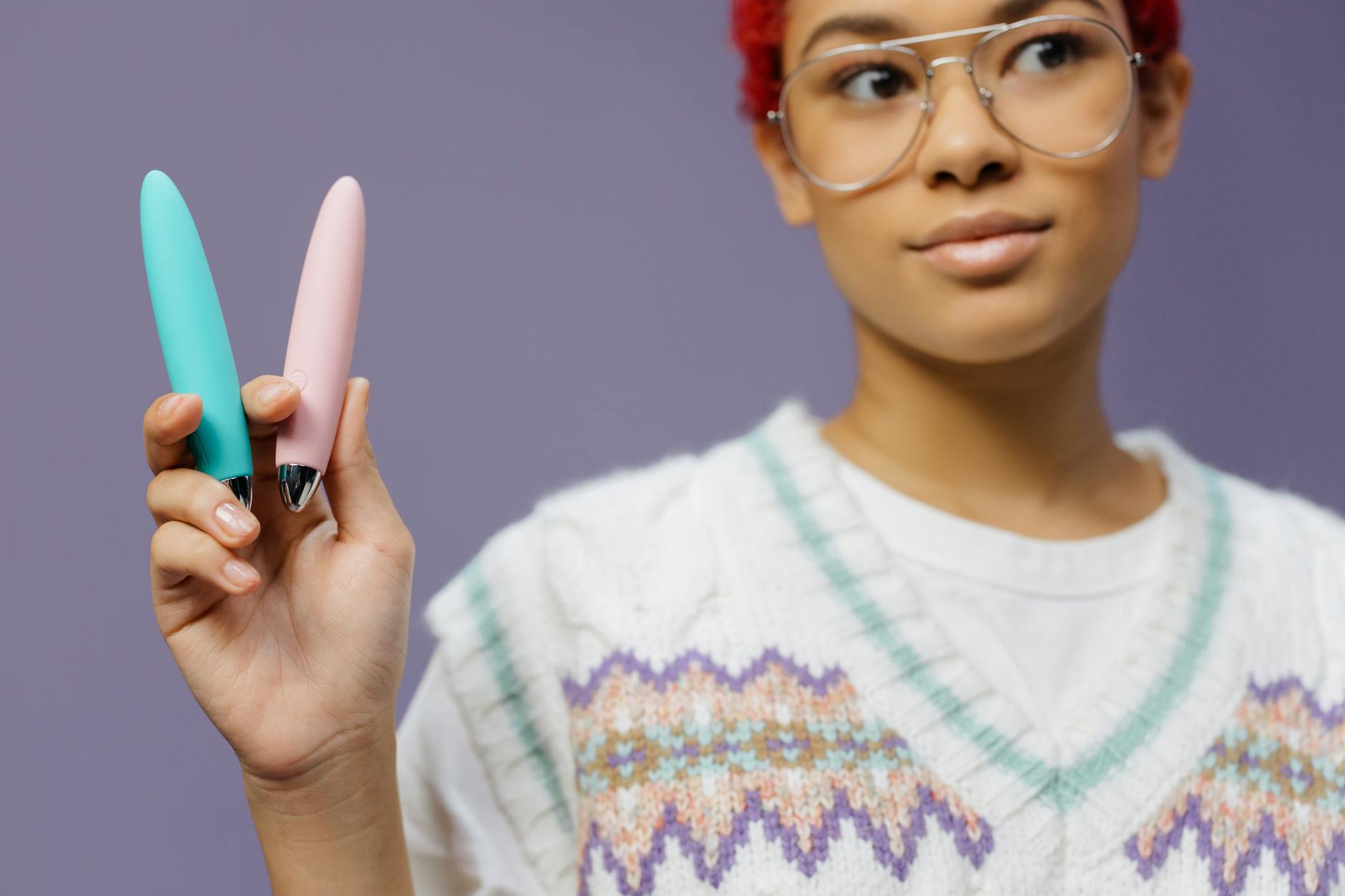 Woman with eyeglasses holds two colorful vibrators