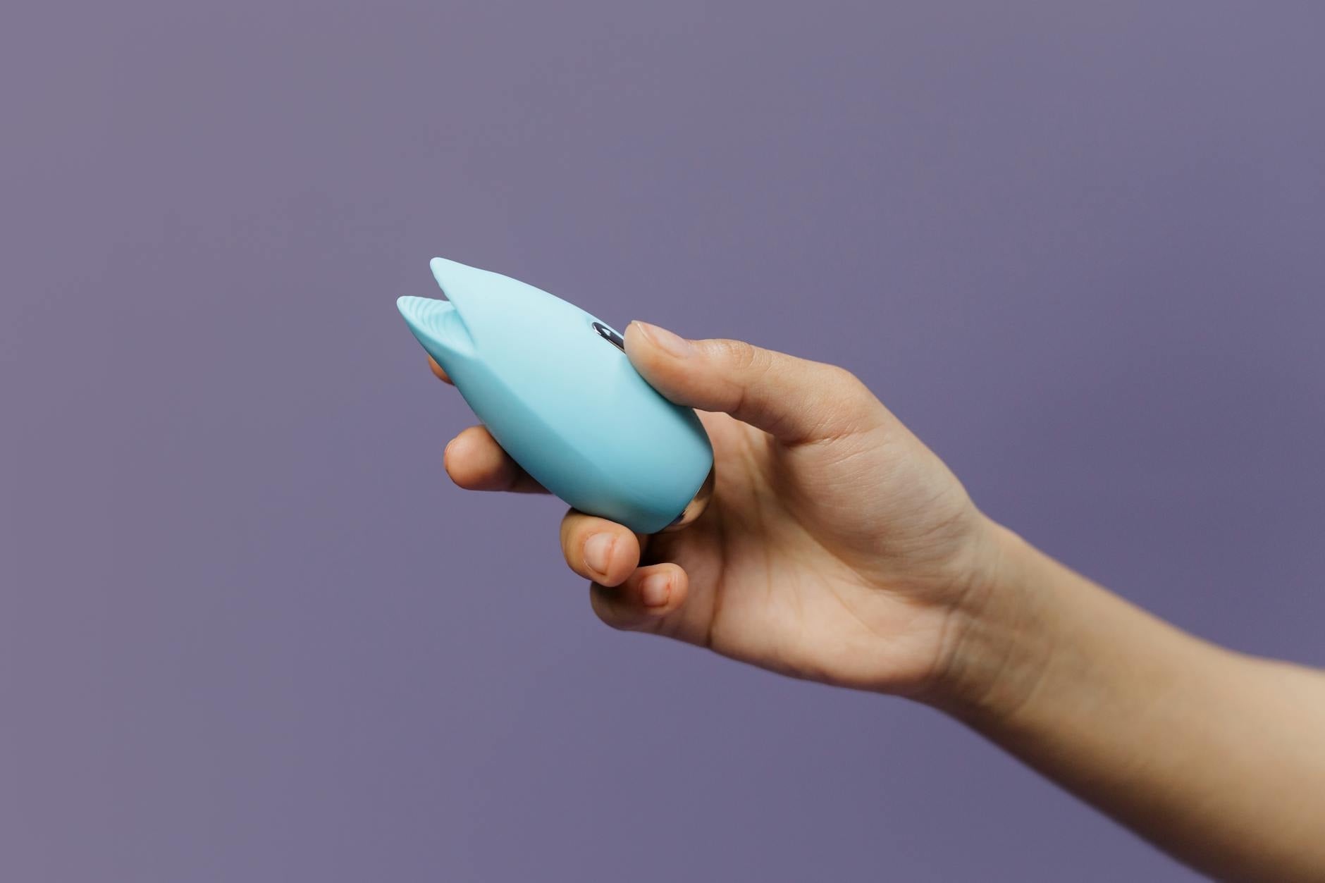 A sleek lemon clitoral vibrator held gently in hand against a purple background