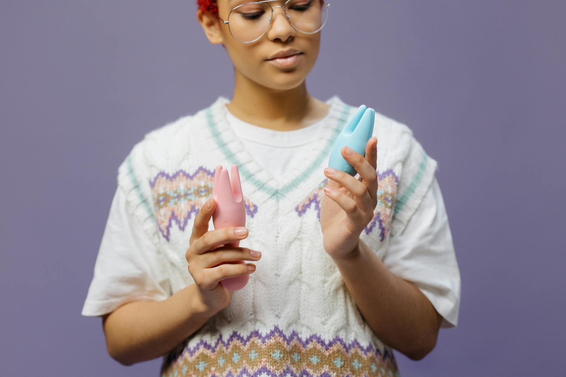 Woman holding blue and pink clitoral vibrators thoughtfully against her chest