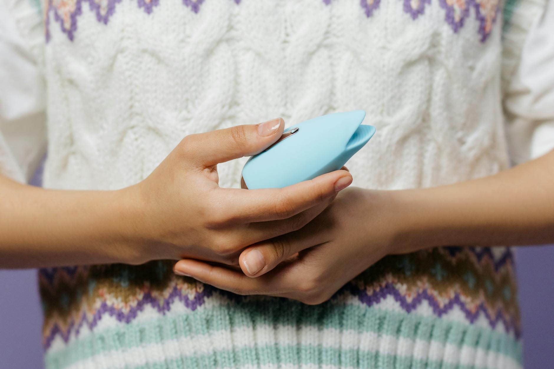 Hands holding a blue personal massager against a soft sweater, showing intimate self-care and pleasure.